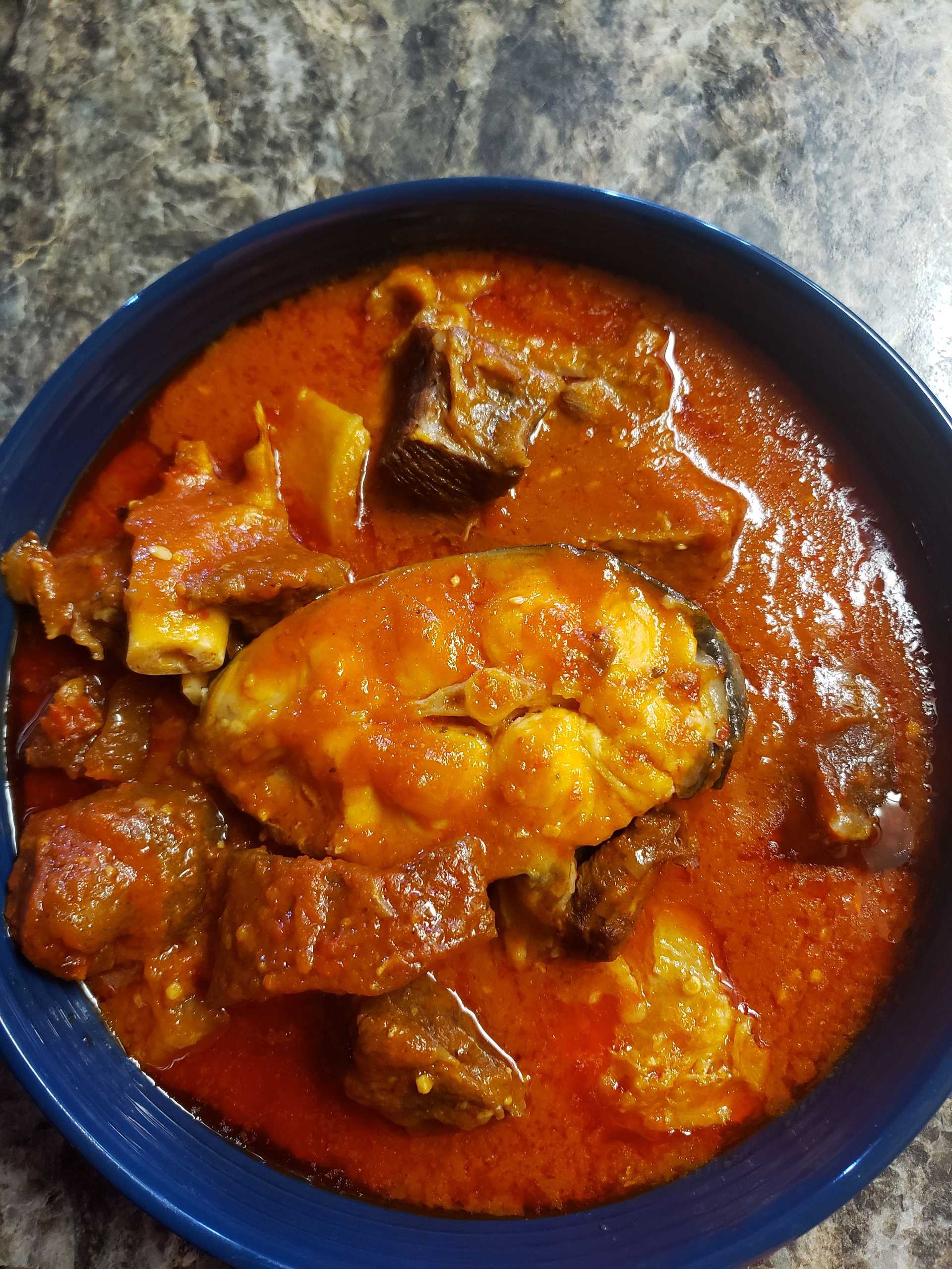 Bowl of spicy stew with meat and seafood on a countertop.