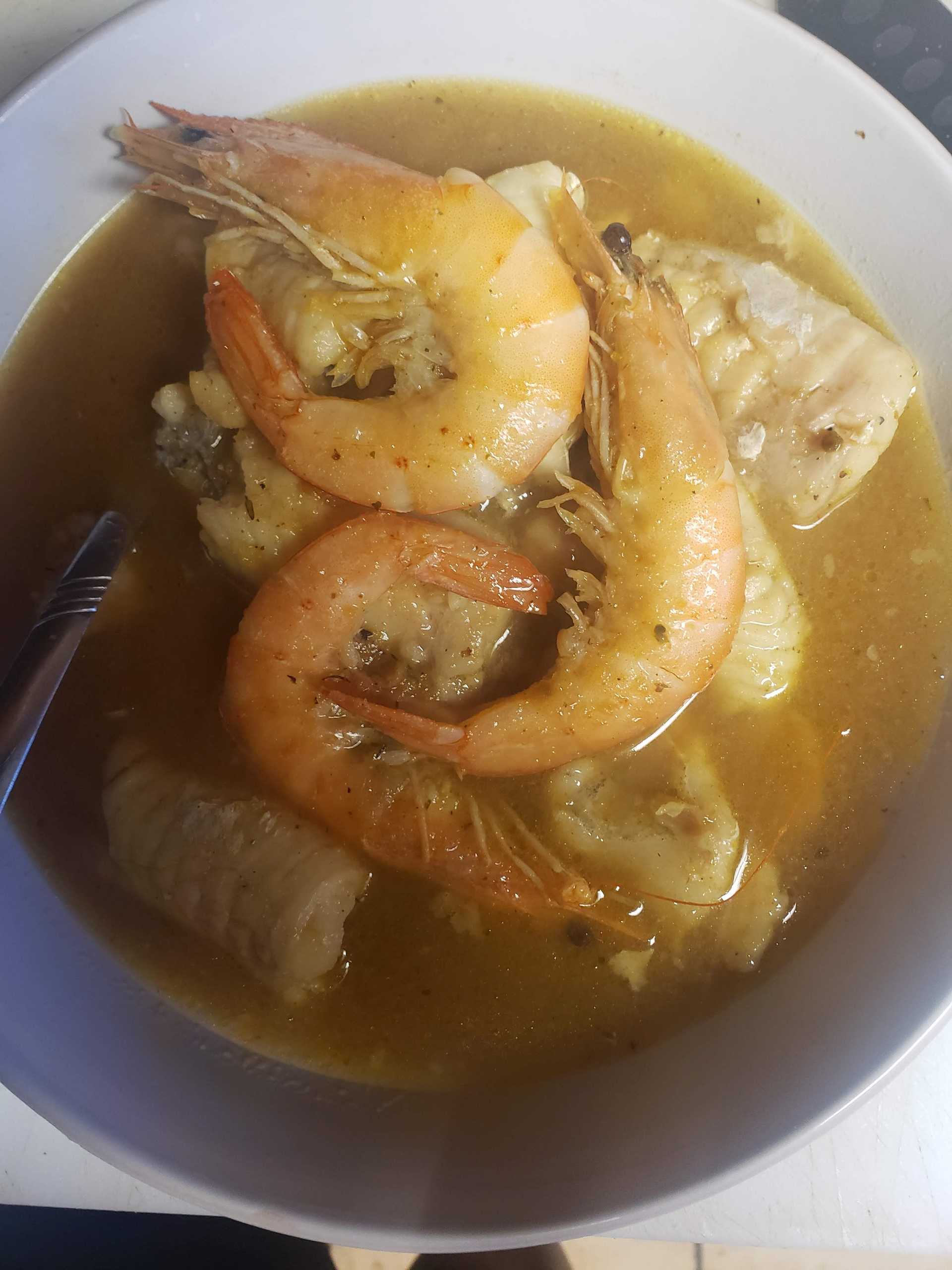 Bowl of seafood gumbo with shrimp and fish, rich in color.