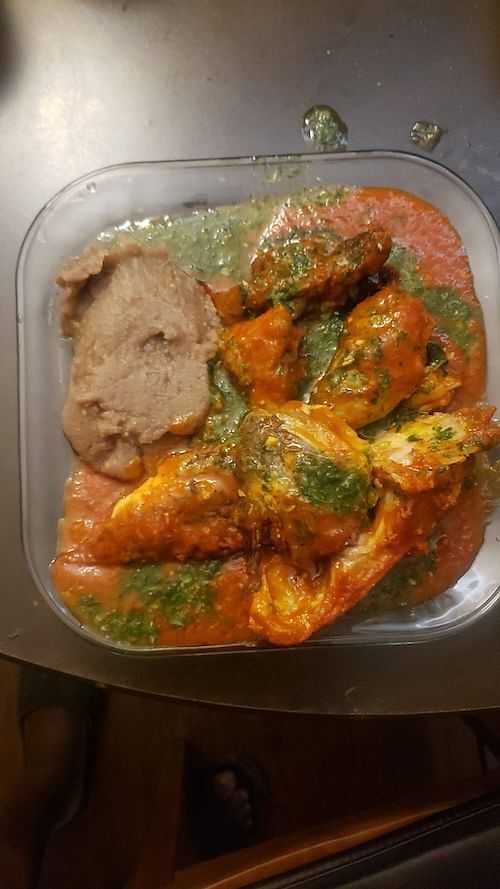 A dish of stewed chicken in tomato sauce with greens and mashed food.
